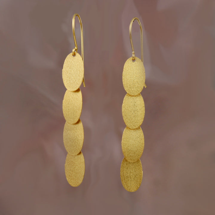 Image of gold, long dangly earrings on a pink background.