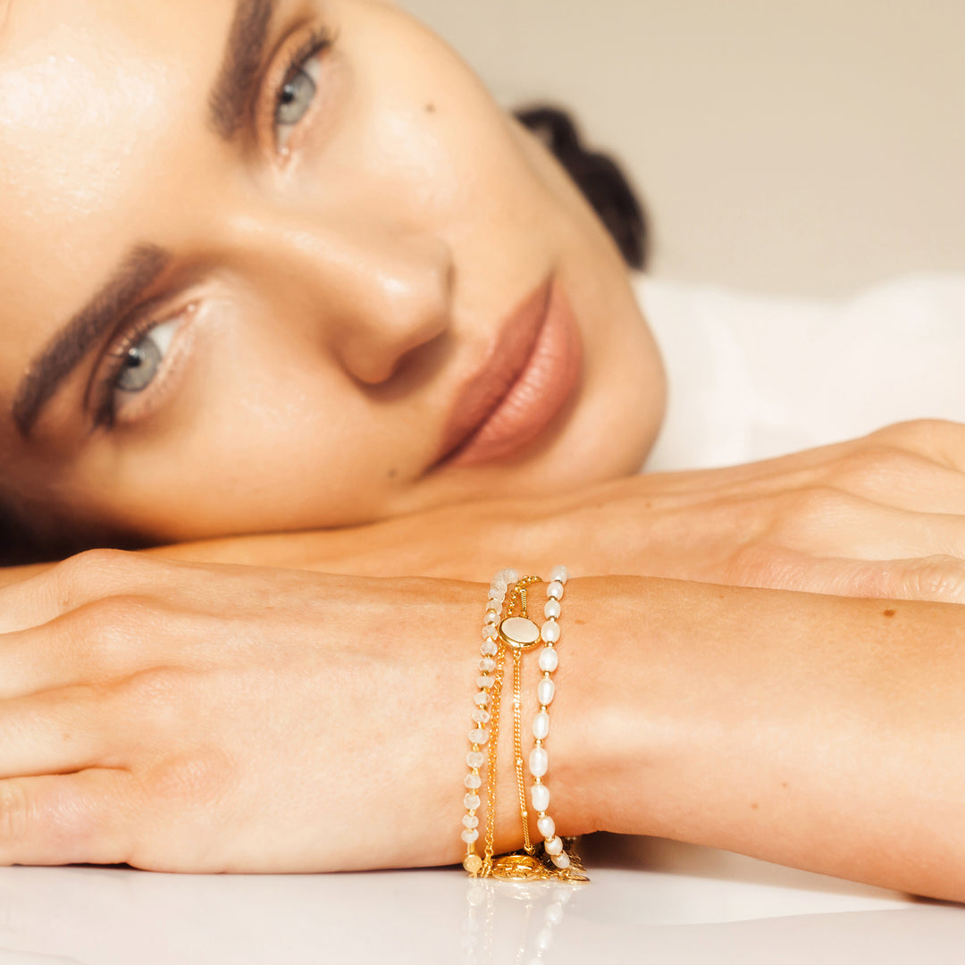 Model wearing gold beaded moonstone and pearl bracelets.