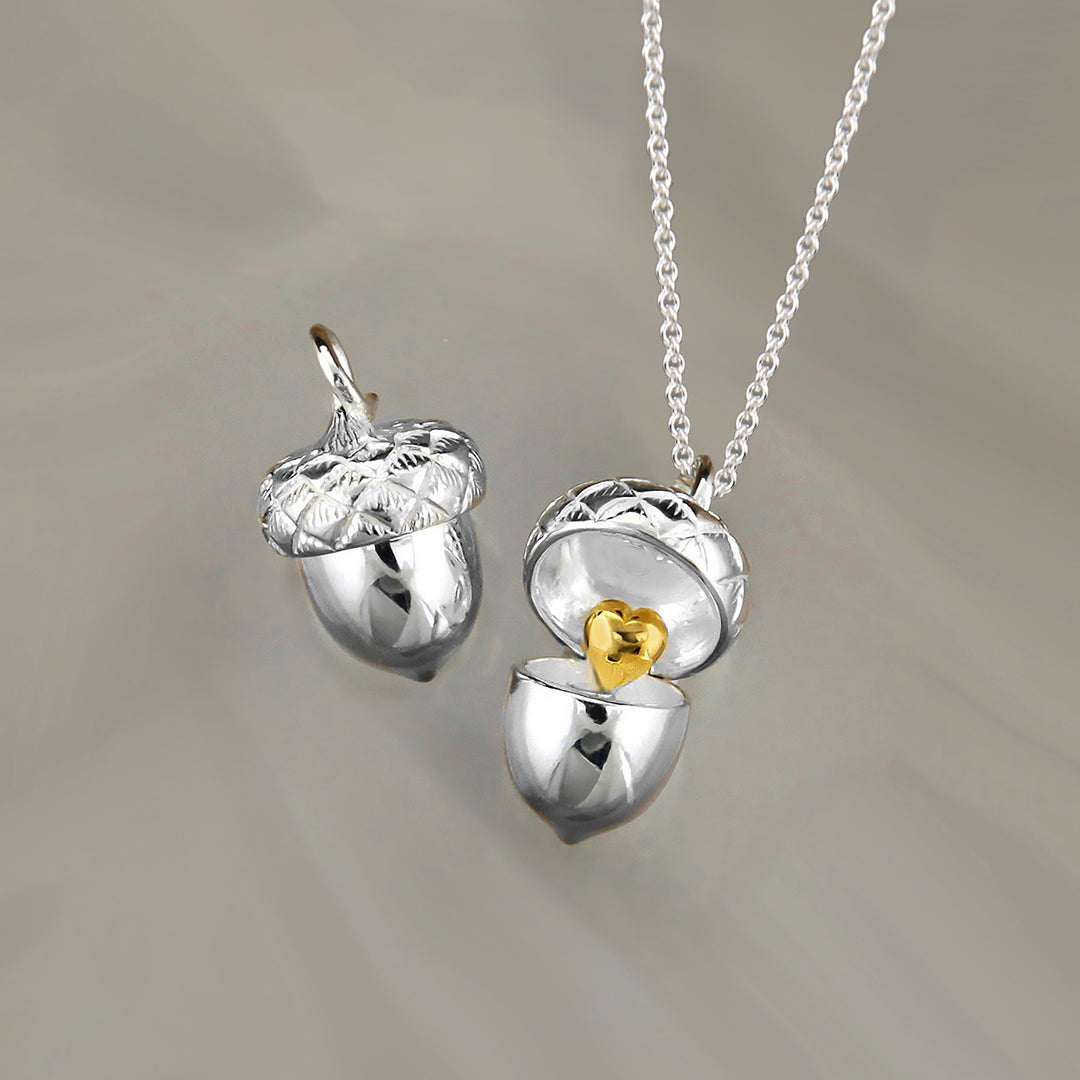 silver acorn locket opening to expose a gold heart with a 2nd closed pendant on gray background