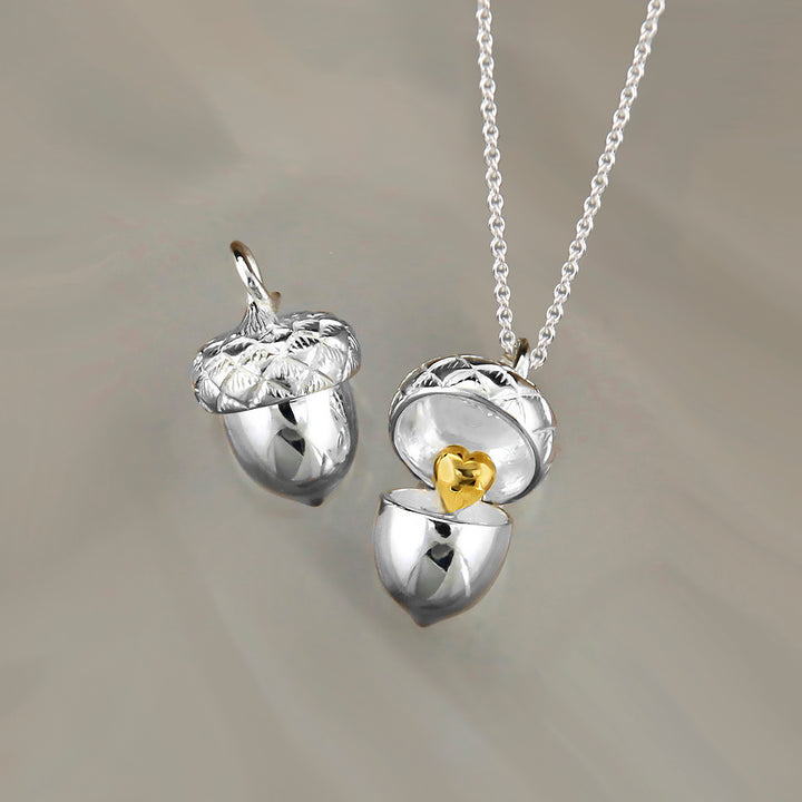 silver acorn locket opening to expose a gold heart with a 2nd closed pendant on gray background
