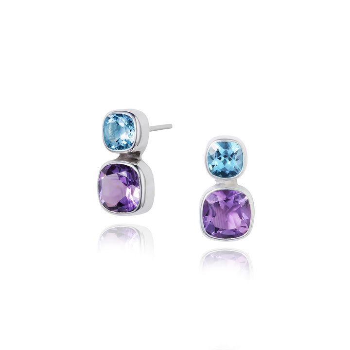 A pair of silver stud earrings featuring  a square amethyst gemstone below a square blue topaz gemstone, set against a white background.